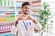© Krakenimages.com - Young hispanic man with tattoos working at pharmacy drugstore smiling in love showing heart symbol and shape with hands. romantic concept.