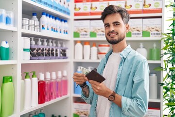 Wall Mural - Young hispanic man customer smiling confident holding dollars at pharmacy