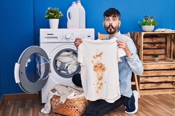 Poster - Young hispanic man with beard holding clean white t shirt and t shirt with dirty stain making fish face with mouth and squinting eyes, crazy and comical.