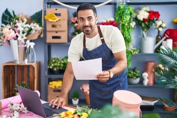 Wall Mural - Young hispanic man florist using laptop reading paper at florist