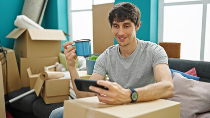 Sticker - Young hispanic man watching video on smartphone drinking coffee at new home