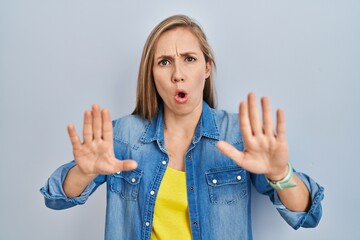 Sticker - Young blonde woman standing over blue background moving away hands palms showing refusal and denial with afraid and disgusting expression. stop and forbidden.