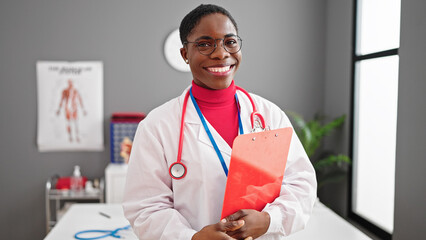 Wall Mural - African american woman doctor smiling confident holding medical report at clinic