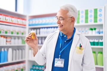 Canvas Print - Middle age grey-haired man pharmacist smiling confident holding pills bottle at pharmacy