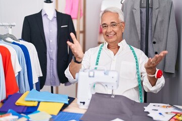 Poster - Middle age man with grey hair dressmaker using sewing machine smiling cheerful offering hands giving assistance and acceptance.