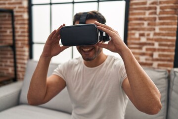 Wall Mural - Young hispanic man playing video game using virtual reality glasses at home