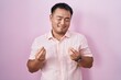 © Krakenimages.com - Chinese young man standing over pink background doing money gesture with hands, asking for salary payment, millionaire business