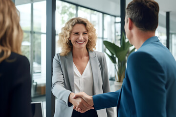 Wall Mural - Happy middle aged business woman meets its client and shakes hands in a modern office. Smiling female executive manager shaking hands with client after making successful deal with partner