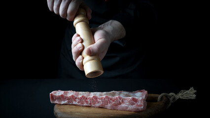 Wall Mural - the chef sprinkles the meat with spices and salt, the concept of the restaurant menu