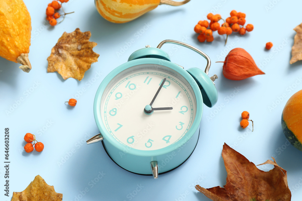 Alarm clock with fallen leaves and berries on blue background, closeup
