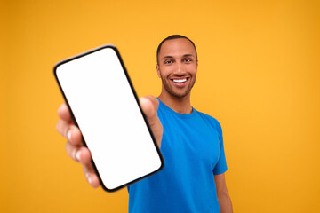 Wall Mural - Young man showing smartphone in hand on yellow background