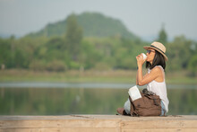 Asian Woman Traveler With Backpack And Cup Of Coffee Sitting On Quayside Relax During Coffee Break On Background Summer Vacations And Lifestyle Hiking Concept.