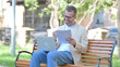 © stockbakers - Middle Aged Man Celebrating while Working on Laptop and Documents Outdoor