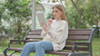 © stockbakers - Casual Young Woman Doing Video Chat on Tablet while Sitting Outdoor on a Bench