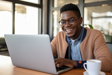 A black young man, laptop in use, wears a bright smile.
