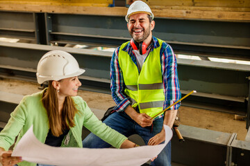 Two happy civil engineer and maintenance engineer in protective vests and helmets working on a construction site