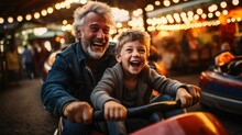 Grandfather And Grandson Smile And Have Fun While Driving A Bumper Car In An Amusement Park.