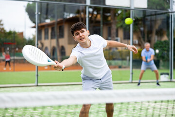 Wall Mural - Focused young man playing paddle tennis couple match at outdoors court