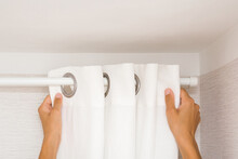 Young adult woman hands hanging clean white thick night curtains in rings on rod at home room. Closeup. Point of view shot. Front view.