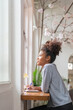 © Natee Meepian - Young African American woman sit on comfortable desk in living room and write down in diary