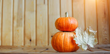 A Pyramid Of Two Orange Pumpkins With A Dry Yellow Maple Leaf On A Wooden Background. Background Concept For Halloween, Thanksgiving And Harvest Day