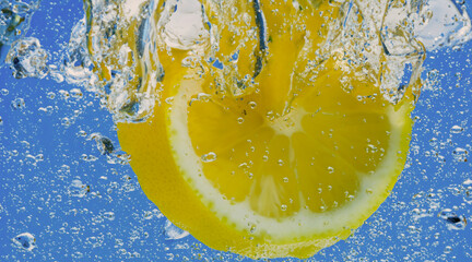 Wall Mural - Underwater lemon slice in soda water or lemonade with bubbles. Refreshing soda tonic fizzy cocktail. Close up of lemons and ice cubes in glass. Lime in splashing sparkling water cold drink beverage.