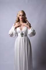 Wall Mural - Close up portrait of beautiful blonde model wearing elegant  white halloween gown, a historical fantasy character.  Holding crucifix cross necklace, isolated on studio background.