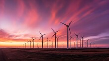 Dynamic Shot Of Wind Turbines In A Row Against A Captivating Sunset Sky With Vibrant Shades Of Orange, Pink, And Purple. Spinning Blades Create Motion Blur, Symbolizing Renewable Energy And Clean Pow