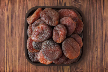 Wall Mural - chocolate dried apricots in square plate on wooden table background. vegetarian organic food for healthy diet.