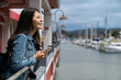 side view of smiling asian Japanese female traveler enjoying fresh air and beautiful view from a waterfront restaurant with phone at Old Fisherman's Wharf in California usa