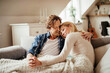 © Geber86 - Middle aged Caucasian couple holding hands under a blanket in the living room