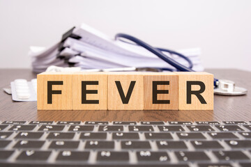 Poster - wooden block form the word FEVER with stethoscope, pills, notepad on the doctor's desktop - medical concept