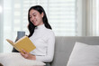 © PaeGAG - Attractive young Asian woman sits in the minimal and comfortable living room enjoying reading a book.