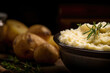 Homemade Thanksgiving mashed potatoes with rosemary in clay ceramic plate, dark background with fresh potatoes. Puree bowl.
