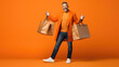 Happy smiling man holding shopping bags on orange background