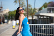 © @skuder_photographer - Young woman from south america with dark hair, wearing a blue dress and sunglasses, leaning back on the railing. She is on holiday in Seville and enjoys the sunny day. Travel and holiday concept.