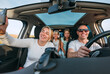© Soloviova Liudmyla - Happy young couple with two daughters inside car during auto trop. They are smiling, laughing and taking selfies using smartphone. Family values, traveling, social media and new technology concepts.