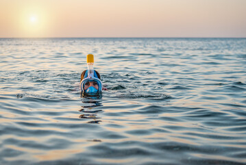 Young woman swimming in the sea with modern snorkeling gear. Full face snorkeling mask. Tropical sea sport activity at sunset