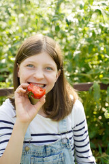 Wall Mural - happy girl eats a red tomato in a greenhouse