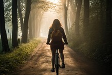Rear View Of A Woman Riding A Bicycle Along A Country Road Among Trees