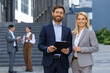 © Liubomir - Portrait of two business partners, business people a man and a woman are smiling and looking at the camera, a businessman and a businesswoman from outside an office building are walking in the city.