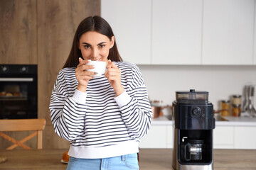 Poster - Young woman drinking hot coffee in kitchen