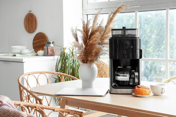 Poster - Modern coffee machine with cup, bun and laptop on table in kitchen