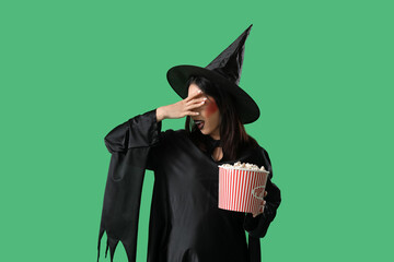 Poster - Scared young Asian woman dressed for Halloween as witch with popcorn on green background