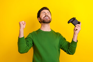 Photo of crazy winner champion best world player young guy fist hold wireless gamepad fifa tournament isolated on yellow color background