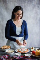 Wall Mural - Mexican adult woman preparing chilaquiles with red sauce traditional mexican food for breakfast in Mexico Latin America, hispanic female cooking