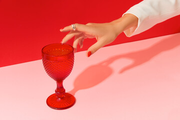 Womans hand with red manicure touches glass on red pink background. Beauty salon concept