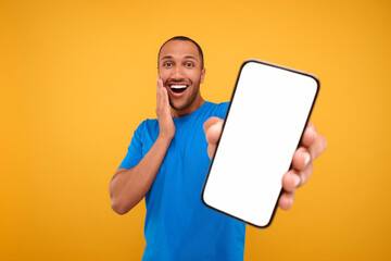 Surprised man showing smartphone in hand on yellow background