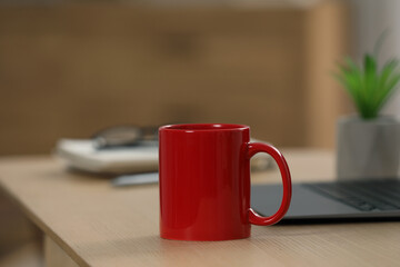 Poster - Red ceramic mug and laptop on wooden table at workplace