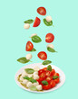 © New Africa - Fresh tomatoes. mozzarella cheese and basil leaves falling onto plate with Caprese salad against turquoise background